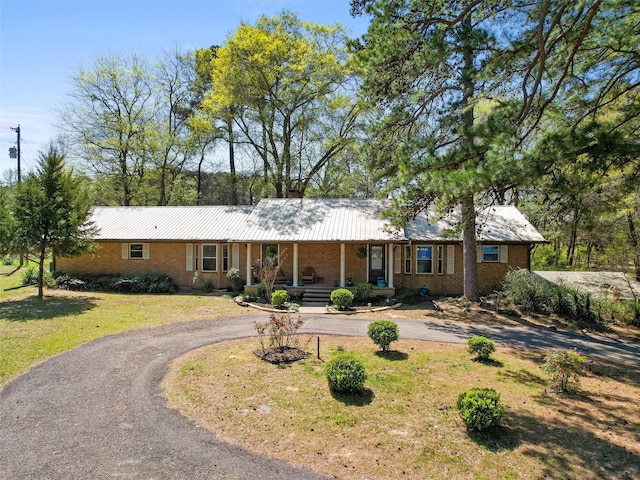 ranch-style home featuring metal roof, brick siding, a front lawn, covered porch, and curved driveway