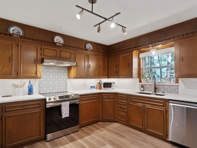 kitchen featuring light countertops, light wood finished floors, appliances with stainless steel finishes, under cabinet range hood, and a sink