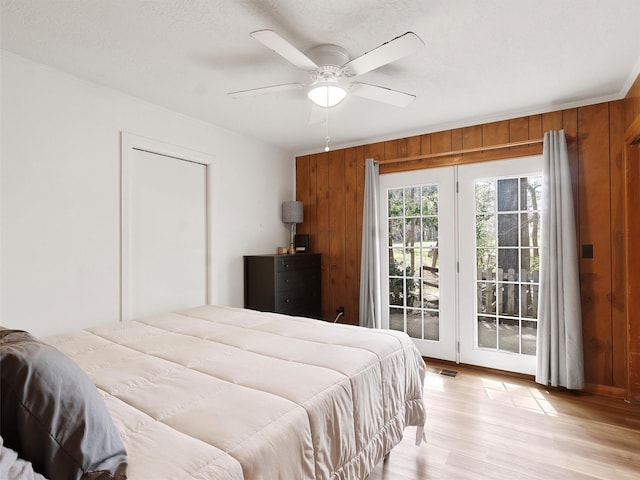 bedroom with access to outside, wooden walls, ceiling fan, light wood-style flooring, and visible vents