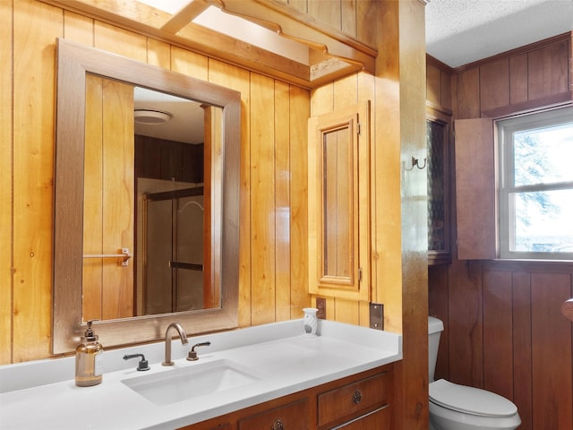 bathroom featuring a shower with door, toilet, vanity, and wood walls