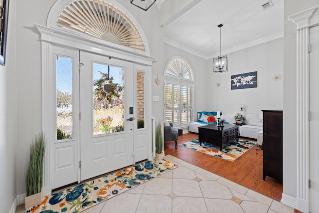 entrance foyer featuring light tile patterned floors, visible vents, crown molding, baseboards, and a notable chandelier
