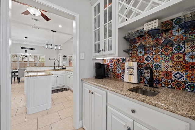 kitchen featuring ceiling fan with notable chandelier, tasteful backsplash, glass insert cabinets, and a sink