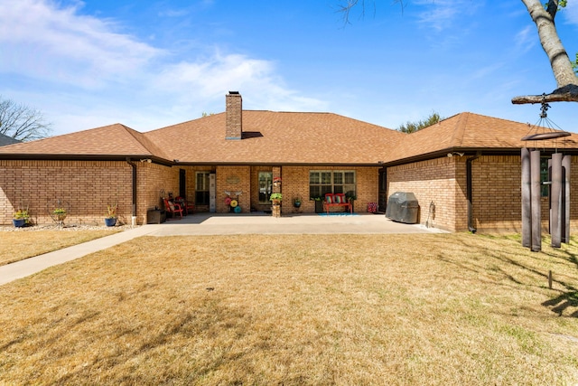 back of property with a patio, a chimney, brick siding, a lawn, and a shingled roof