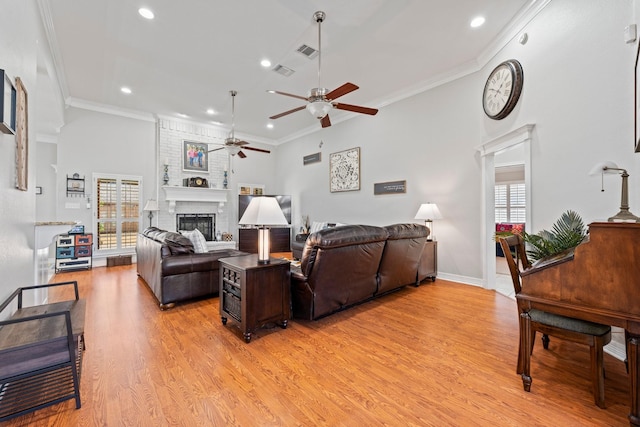 living room featuring light wood-type flooring, ornamental molding, visible vents, a brick fireplace, and ceiling fan