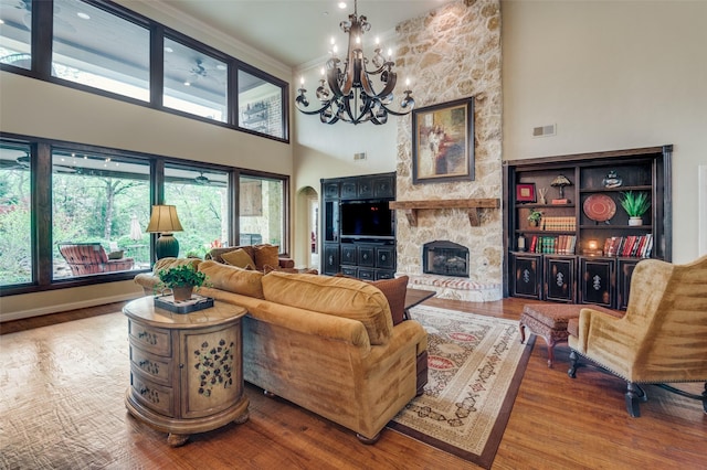 living area featuring a towering ceiling, an inviting chandelier, visible vents, wood finished floors, and a fireplace