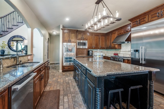 kitchen featuring arched walkways, a sink, built in appliances, light stone counters, and under cabinet range hood