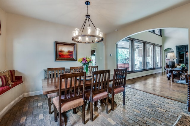dining area featuring arched walkways, a notable chandelier, brick floor, and baseboards