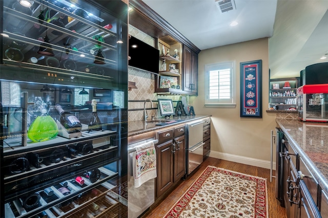 kitchen featuring wood finished floors, visible vents, a sink, baseboards, and decorative backsplash