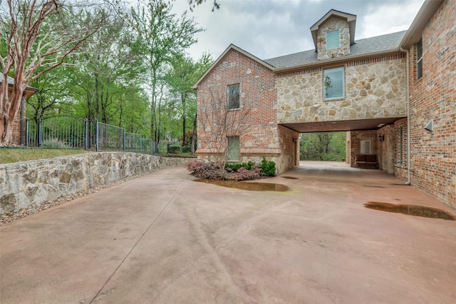 view of home's exterior with driveway, a carport, stone siding, and fence