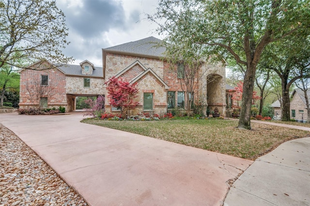 view of front facade with brick siding, a front lawn, driveway, and stone siding
