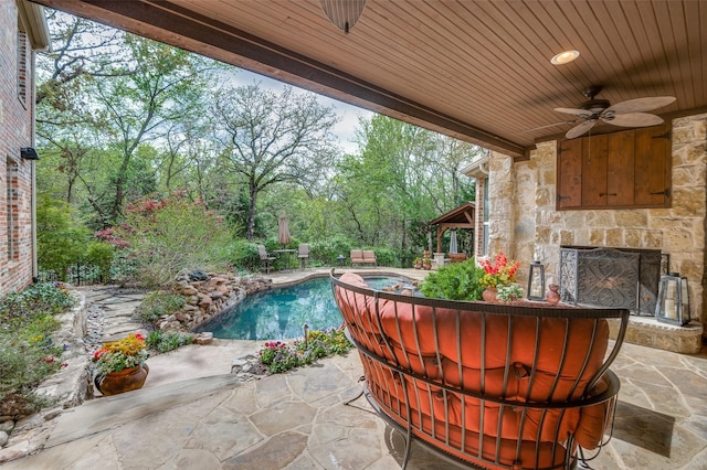 view of patio featuring an outdoor pool, an outdoor stone fireplace, and a ceiling fan