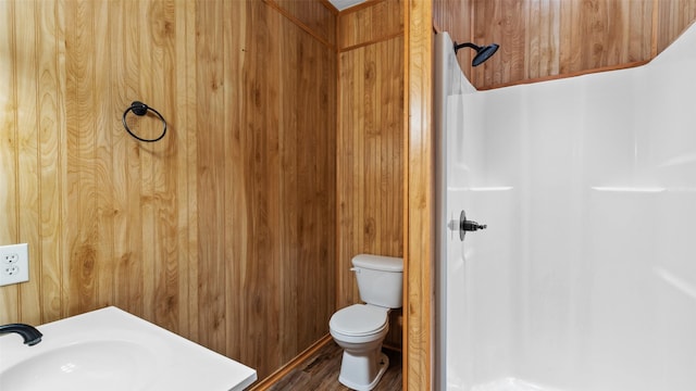full bath featuring a shower, wood walls, toilet, a sink, and wood finished floors