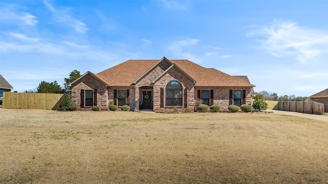 view of front facade featuring brick siding, a shingled roof, and fence