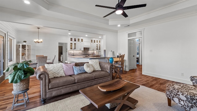 living room with crown molding, ceiling fan with notable chandelier, baseboards, a raised ceiling, and dark wood-style floors