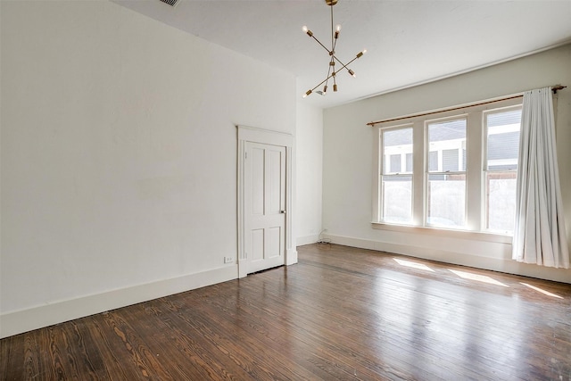 empty room featuring dark wood-type flooring, baseboards, and a chandelier