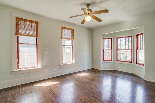 unfurnished room featuring a wealth of natural light, baseboards, dark wood-type flooring, and a ceiling fan