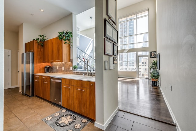 2323 N Houston St Unit 710, Dallas, TX 75219 - kitchen featuring appliances with stainless steel finishes, brown cabinetry, healthy amount of natural light, a high ceiling, and light countertops