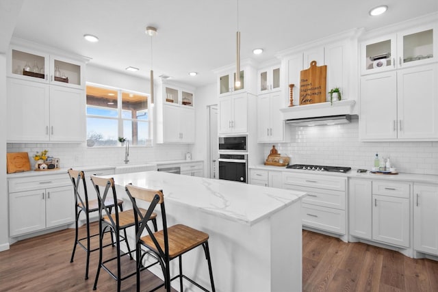kitchen featuring gas cooktop, stainless steel oven, white cabinetry, built in microwave, and a breakfast bar area