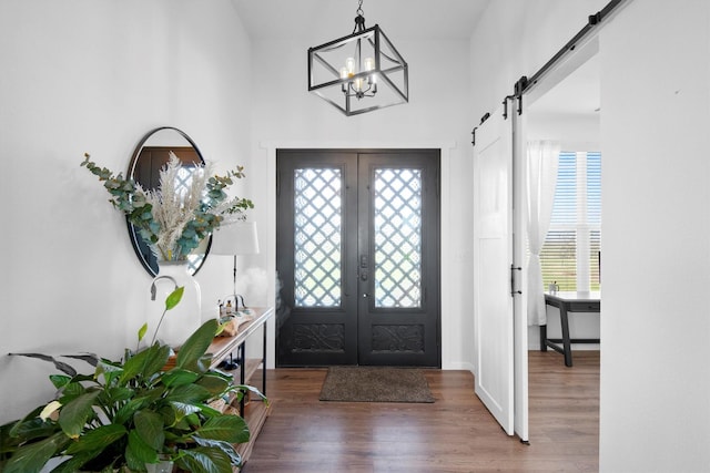 foyer entrance with french doors, a notable chandelier, a barn door, and wood finished floors