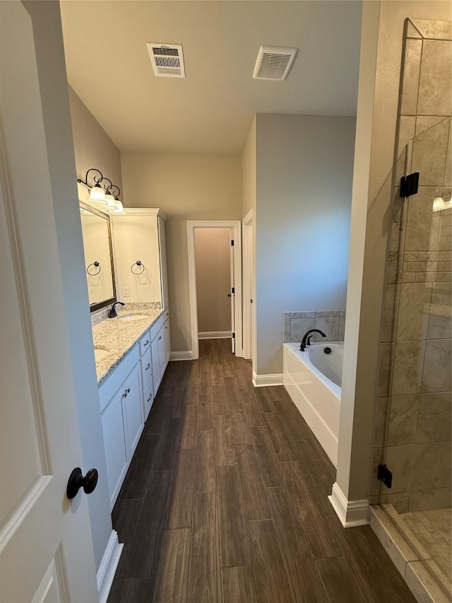 bathroom featuring double vanity, visible vents, wood finished floors, a sink, and a bath