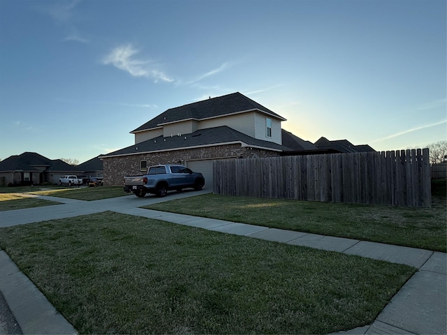 view of side of property with brick siding, a lawn, concrete driveway, and fence