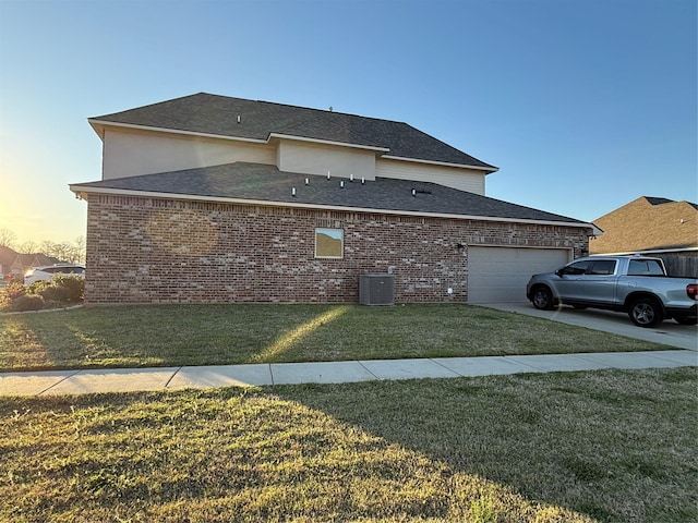 property exterior at dusk with cooling unit, brick siding, an attached garage, a shingled roof, and a yard