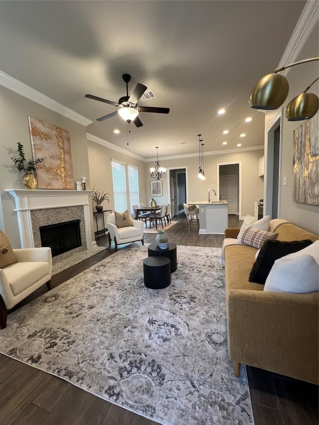 living area featuring crown molding, ceiling fan with notable chandelier, a fireplace with flush hearth, dark wood-style flooring, and recessed lighting