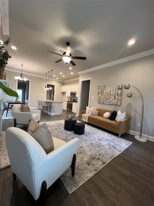 living room with baseboards, recessed lighting, ornamental molding, and ceiling fan with notable chandelier