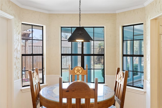 dining space featuring a textured wall, a healthy amount of sunlight, and a wainscoted wall