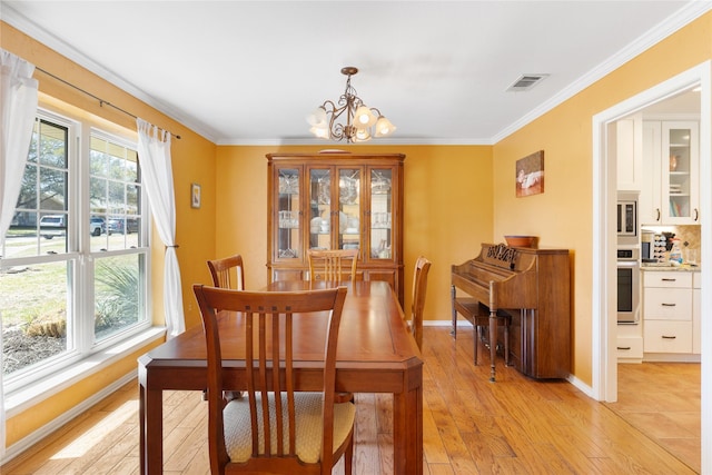 dining area featuring visible vents, crown molding, baseboards, light wood-style flooring, and a notable chandelier