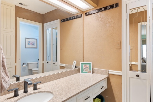 bathroom with visible vents, a textured wall, toilet, and vanity