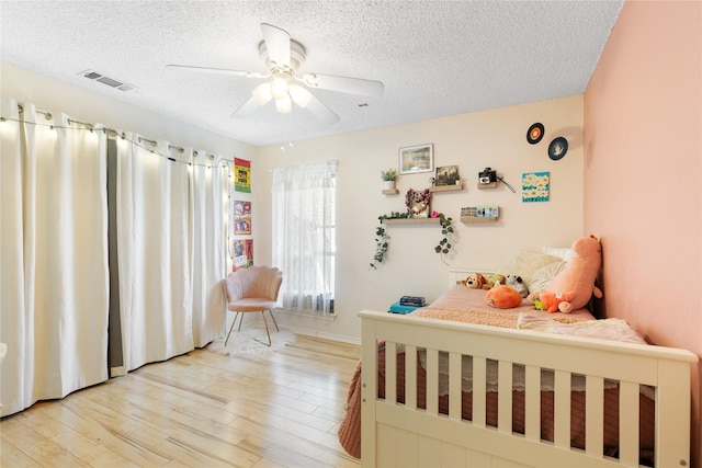 bedroom featuring a textured ceiling, visible vents, ceiling fan, and light wood finished floors