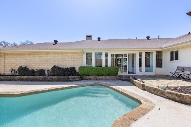 rear view of house with a fenced in pool, a patio, and brick siding