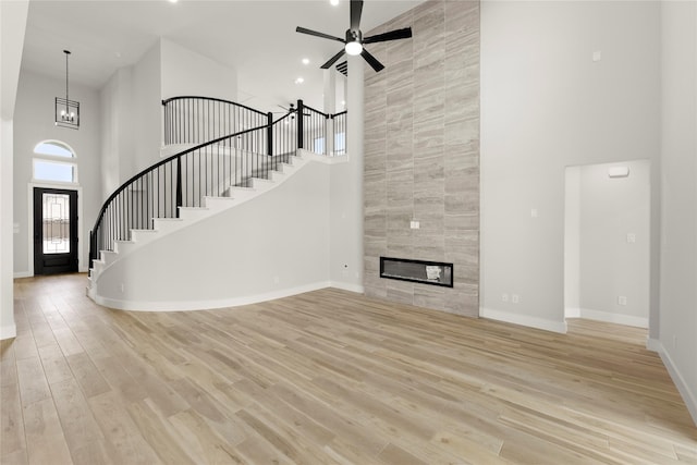 unfurnished living room with stairs, baseboards, a towering ceiling, light wood-style floors, and ceiling fan