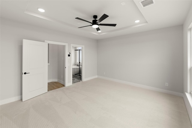 unfurnished bedroom featuring a tray ceiling, carpet floors, baseboards, visible vents, and recessed lighting