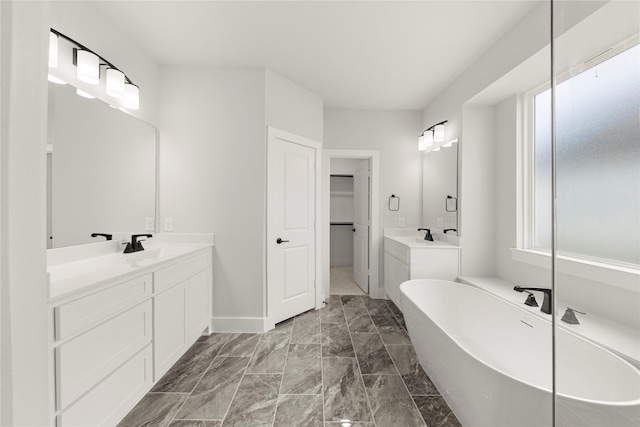 bathroom featuring a spacious closet, baseboards, a sink, a freestanding bath, and two vanities