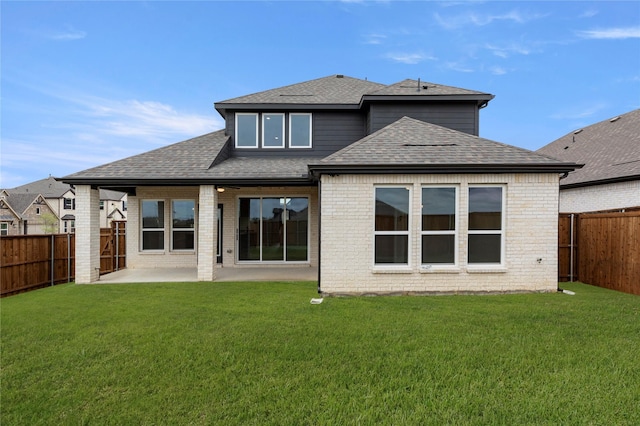 back of house with a yard, a fenced backyard, roof with shingles, and a patio area