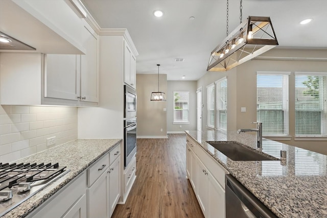 kitchen with wood finished floors, white cabinets, tasteful backsplash, a sink, and appliances with stainless steel finishes