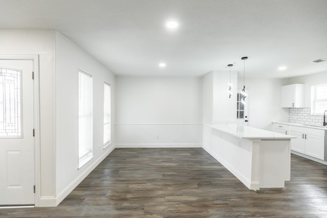 kitchen featuring dark wood-style flooring, white cabinets, a peninsula, tasteful backsplash, and a sink