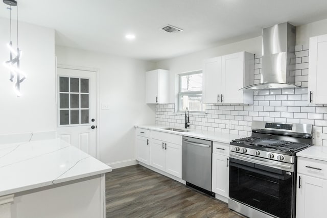 kitchen featuring decorative backsplash, wall chimney exhaust hood, stainless steel appliances, a sink, and dark wood-style floors