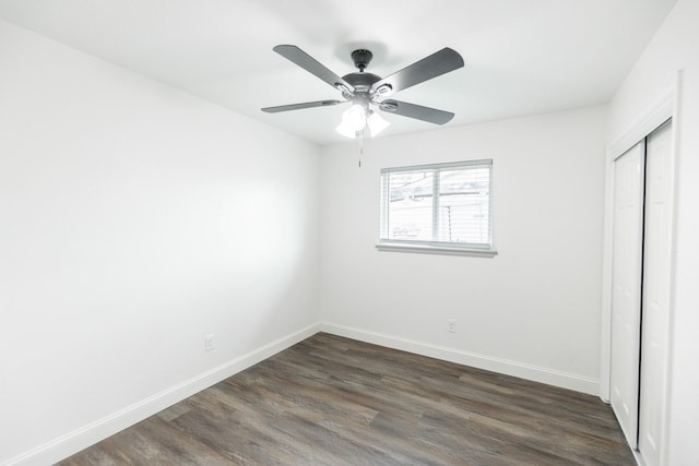 unfurnished bedroom featuring dark wood-style floors, a closet, baseboards, and a ceiling fan