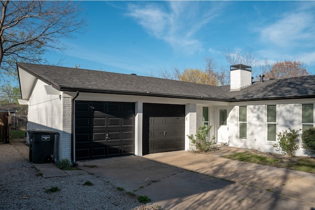 view of front facade with roof with shingles, concrete driveway, a chimney, an attached garage, and brick siding