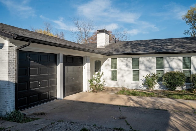 exterior space featuring a chimney, a garage, brick siding, driveway, and a shingled roof