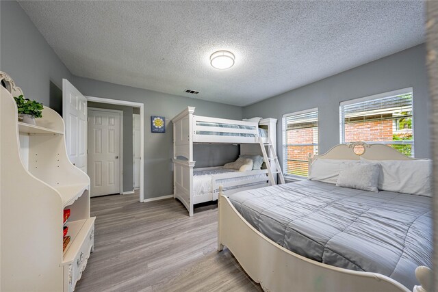 bedroom with baseboards, light wood-style floors, a textured ceiling, and visible vents