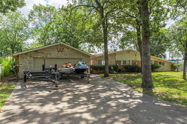 view of front of home with driveway, an attached garage, stone siding, and a front lawn