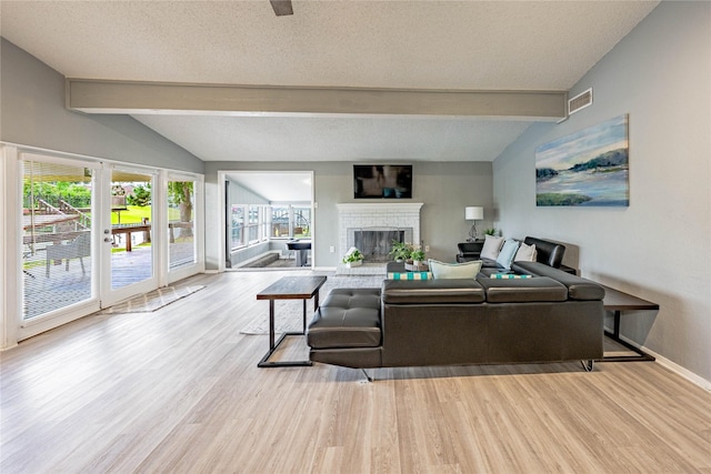 living area with a textured ceiling, baseboards, a fireplace, wood finished floors, and vaulted ceiling with beams