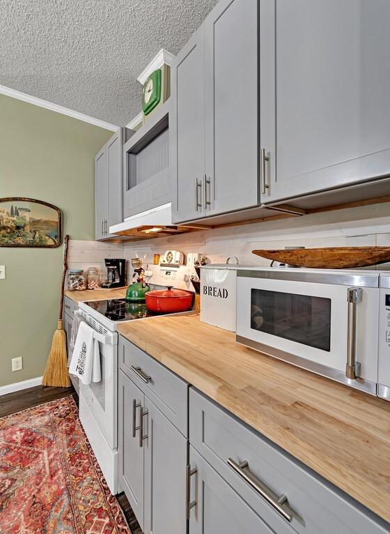 kitchen featuring crown molding, white appliances, butcher block counters, a textured ceiling, and open shelves
