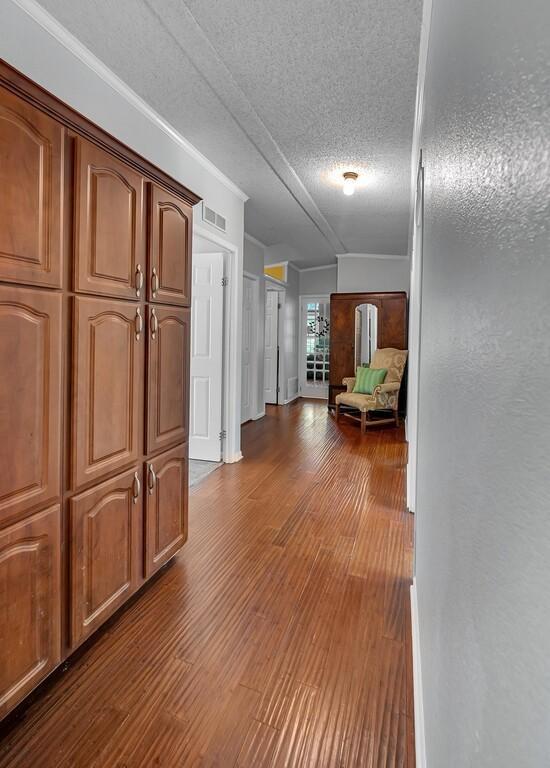 corridor featuring dark wood-type flooring, a textured ceiling, baseboards, and visible vents