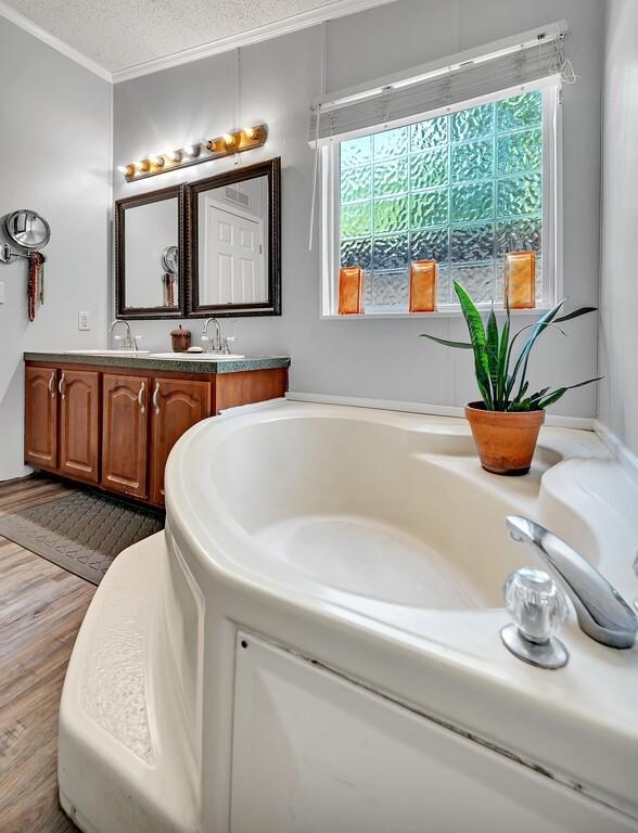 bathroom featuring a garden tub, a textured ceiling, ornamental molding, wood finished floors, and double vanity