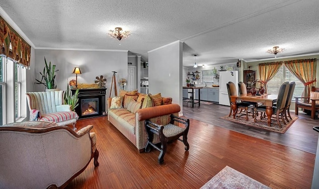 living room featuring a glass covered fireplace, a textured ceiling, crown molding, and wood finished floors